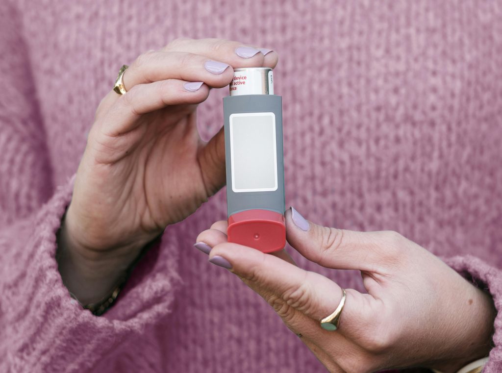 Female hands holding an asthma inhaler with a pink sweater background.